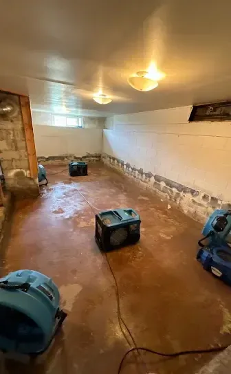 Air movers lined up across a basement floor during a water damage dry-out