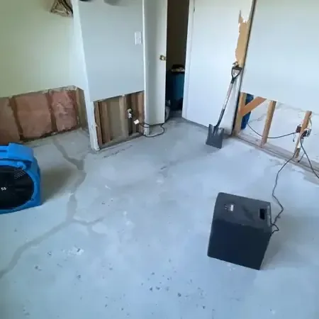 Technician placing an air mover beside a wet wall while a dehumidifier runs in the corner of a room
