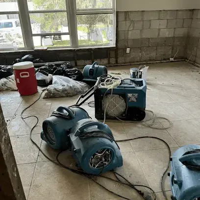 Air movers and a dehumidifier running on the tile floor of a gutted room